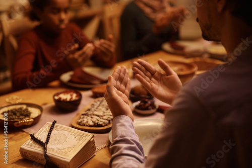 Close up of Muslim man praying with his family at dining table.