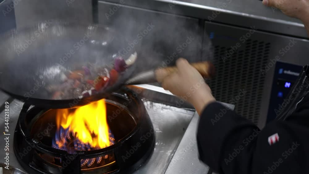 Chef in a restaurant kitchen stir fry meat and vegetables in a wok Chef in a restaurant kitchen stir fry meat and vegetables in a wok