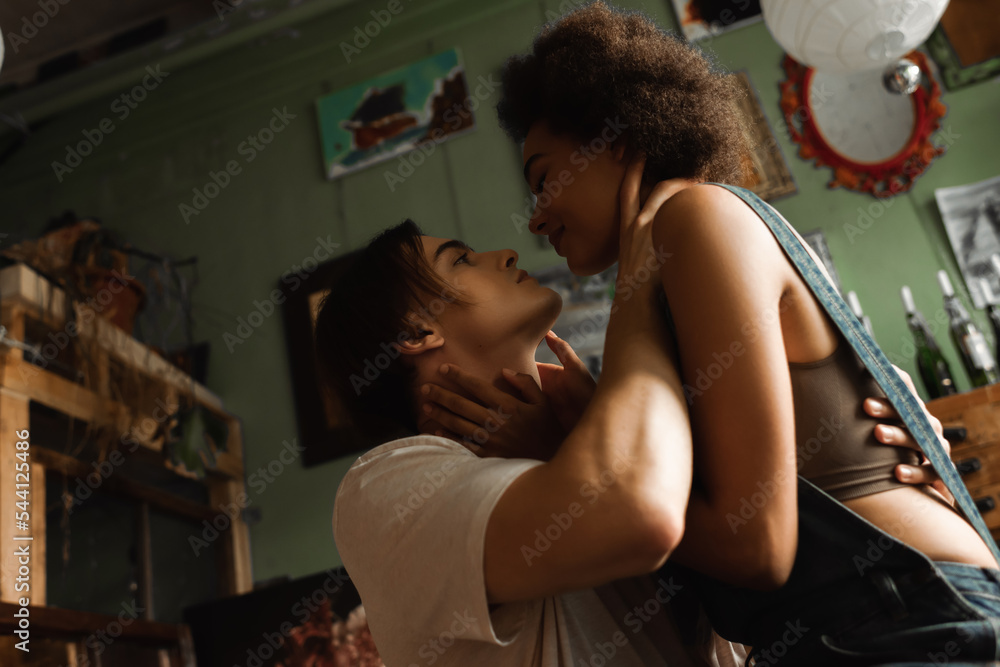 Obraz premium passionate multiethnic couple embracing and looking at each other in art workshop.