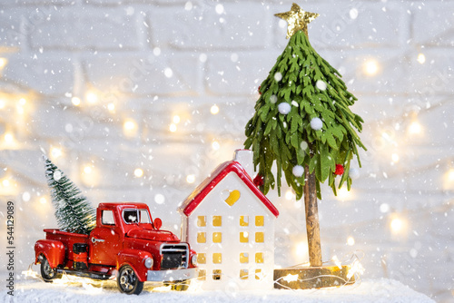 Christmas decor red retro car pickup truck on snow with fairy lights in bokeh Christmas tree. New Year greeting card. Cozy home