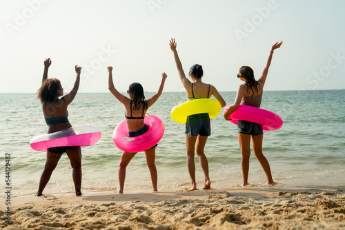 Back of teeage girls with pink and yellow swimming ring look at the sea and enjoy with dancing together on the beach during holiday or vacation. photo