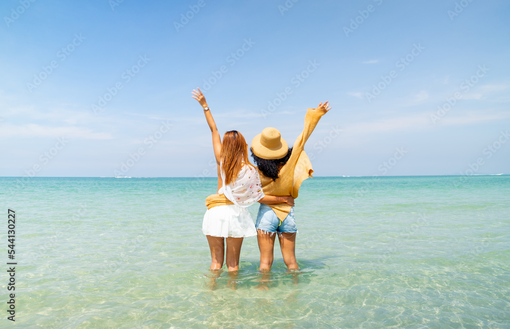 Back of couple women stand with wave hands out to sea with happiness and enjoy holiday together at beach with day light and relax time. Back of couple women stand with wave hands out to sea with happiness and enjoy holiday together at beach with day light and relax time.