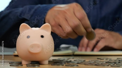 4K-UHD Slow motion of man hand putting coins in pink piggy bank and writing for account save money. Planning step up, saving money for future plan, retirement fund. Business investment-finance