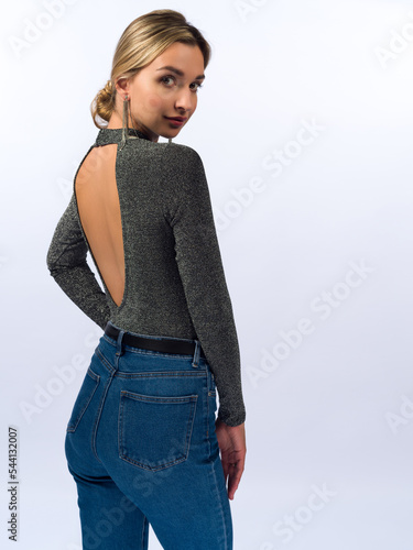 A beautiful, young, slender girl with long blonde hair on a white background in blue jeans and a tight-fitting jacket.