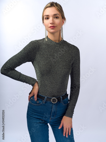 A beautiful, young, slender girl with long blonde hair on a white background in blue jeans and a tight-fitting jacket.