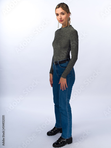 A beautiful, young, slender girl with long blonde hair on a white background in blue jeans and a tight-fitting jacket. Full height