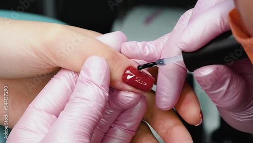 Manicurist applies top coat on nails with red gel polish