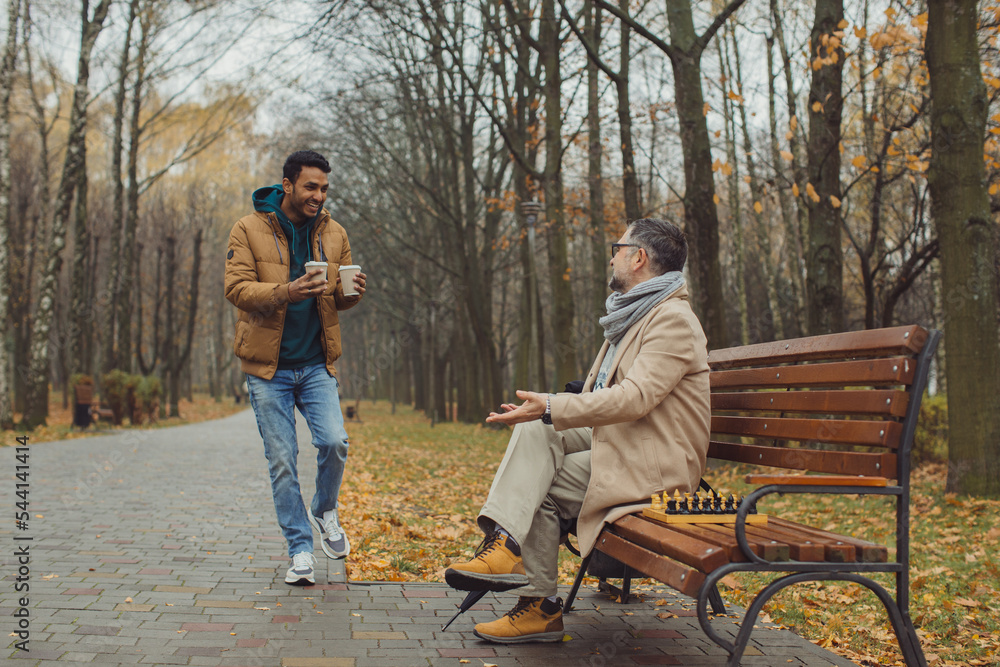 Multicultural friendship of people of different ages. A meeting of two friends for a game of chess in the park. Multicultural friendship of people of different ages. A meeting of two friends for a game of chess in the park.