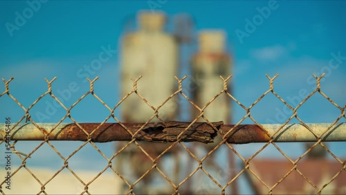 Chain link fence close up with concrete mixing towers in background- timelapse