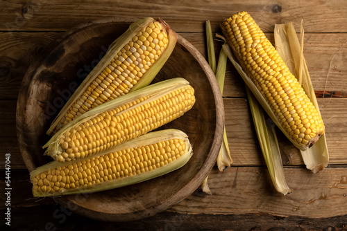 Vista cenital de Mazorcas de maíz dulce (Zea mays) en un plato de madera sobre mesa rústica photo