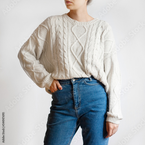 Woman wearing white chunky sweater and blue jeans isolated on white background.