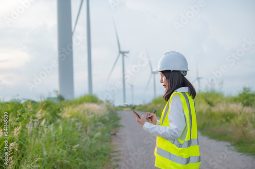 women engineer working and holding the report at wind turbine farm Power Generator Station on mountain,Thailand people