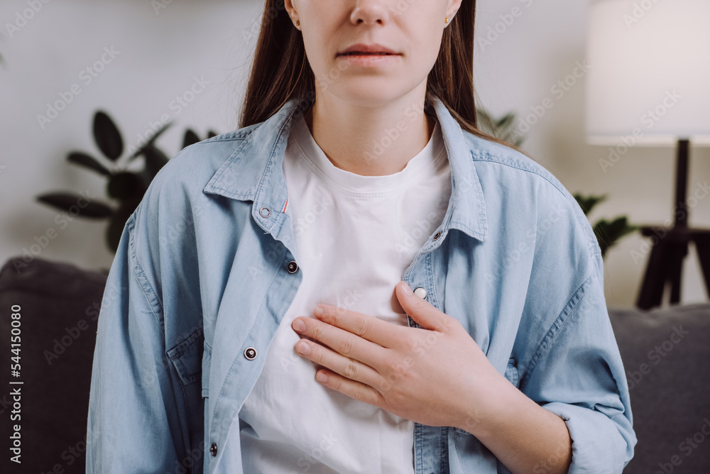 Closeup of upset unhealthy young female sitting on grey sofa at home
