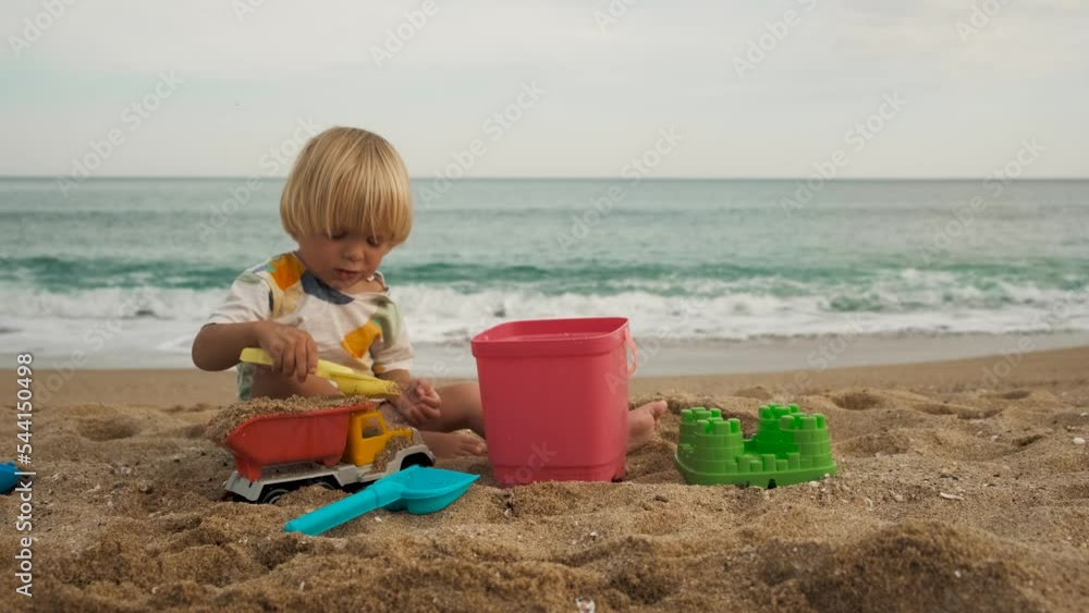 Close-up of a child playing with a shovel and bucket on the sand at the beach Close-up of a child playing with a shovel and bucket on the sand at the beach