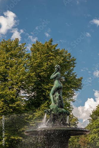 Helsinki, Finland - July 19, 2022: Closeup of female, Havis Amanda statue in fountain and at Market Square in Kaartinkaupunki under blue sky. Green foliage in back. 
