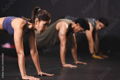 Young group of Asian male and female friends in sportswear clothing working out in advanced plank pose on palms together while on modern gym and fitness club on floor and talking to each other