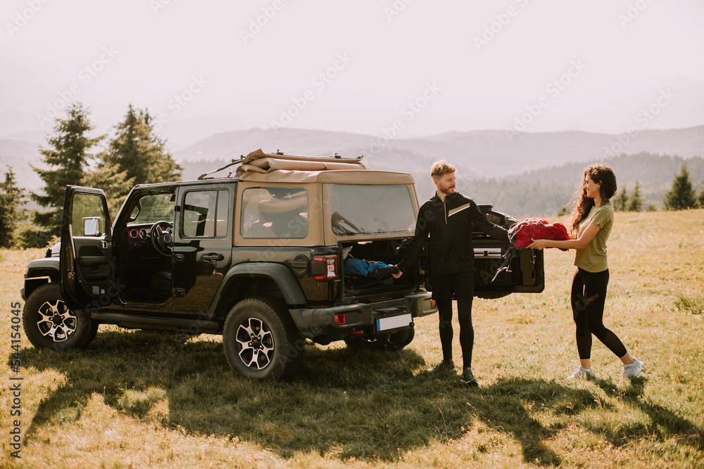 Obraz premium Smiling couple preparing hiking adventure with backpacks by terrain vehicle