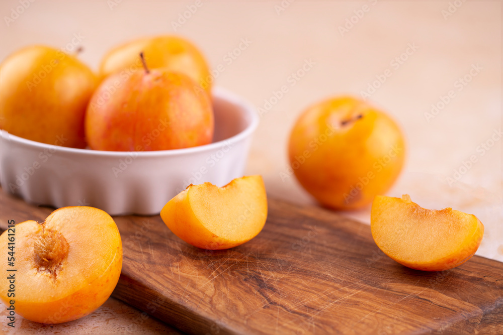 Close-up of yellow plums in a white bowl whole and pieces on a wooden board on the table. Copy space, placement