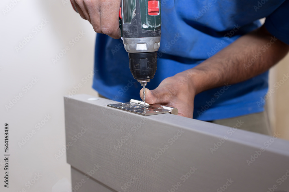 A carpenter drills a hole in a wooden board with an electric drill.