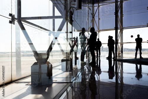 View from inside an airport of silhouettes of unrecognizable people on the facade looking towards the runway