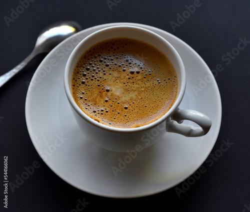 Juicy freshly brewed coffee with foam in a white cup on a black background. Beautiful cup of coffee close-up from above.