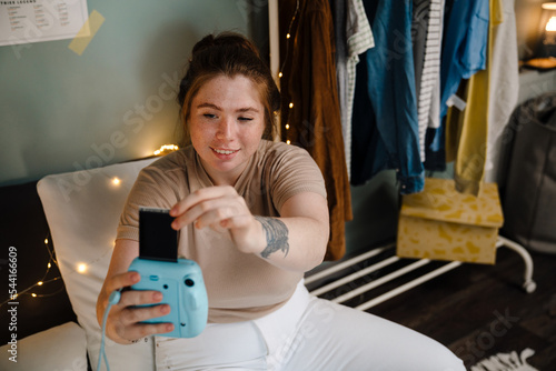 Young beautiful smiling girl taking out selfpicture from polaroid photo