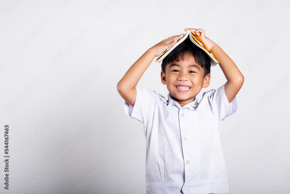 Asian adorable toddler smiling happy wearing student thai uniform red pants stand holding book over head like roof in studio shot isolated on white background, Portrait little children boy preschool Asian adorable toddler smiling happy wearing student thai uniform red pants stand holding book over head like roof in studio shot isolated on white background, Portrait little children boy preschool