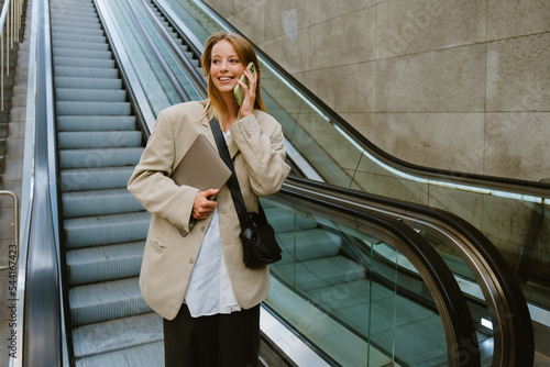 Young woman talking on cellphone while going down escalator outdoors
