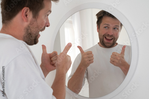 Man trying to encourage himself showing thumb up looking in mirror.  photo