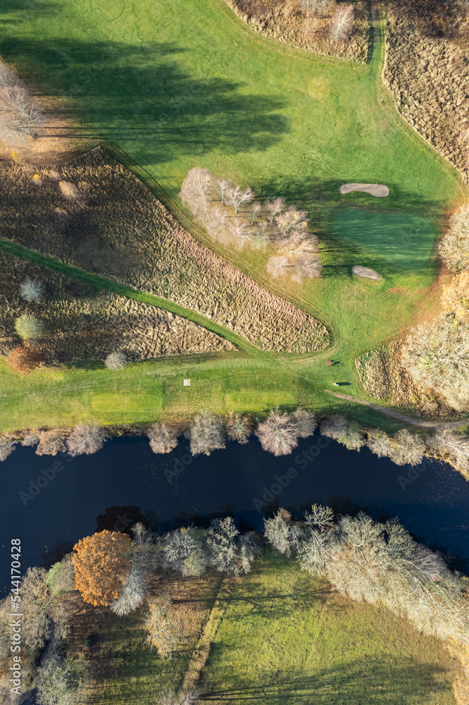 Aerial panoramic view of beautiful autumn morning, golf course, river, multicolored trees and green grass, warm sunlight, shadows