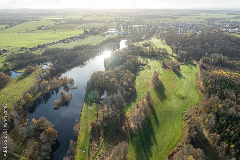Aerial panoramic view of beautiful autumn morning, golf course, river, multicolored trees and green grass, warm sunlight, shadows