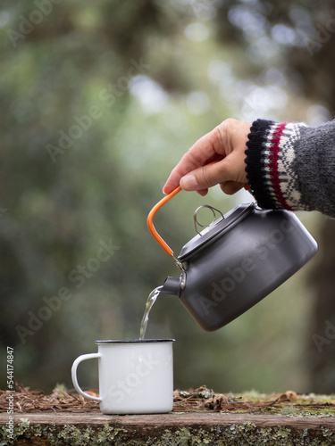 Fototapet pouring hot water from metal teapot into a enamel vintage cup at wooden table ou