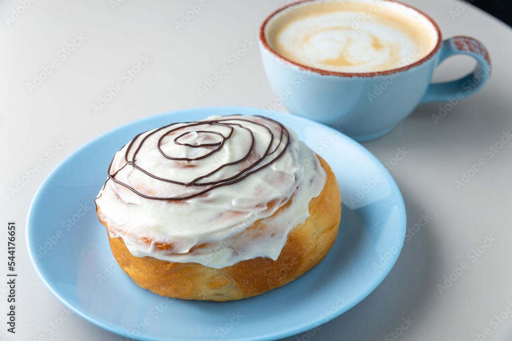Donut covered with icing sugar and chocolate topping on blue plate and cup of cappuccino Donut covered with icing sugar and chocolate topping on blue plate and cup of cappuccino