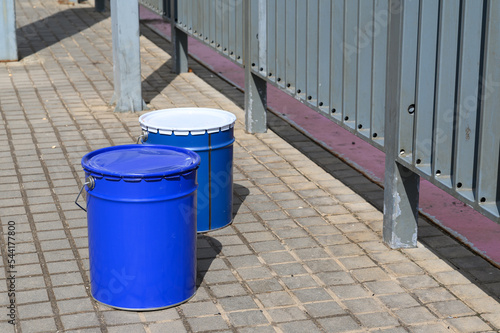 a large blue bucket with white paint stands on the concrete floor on the construction site. © spritnyuk