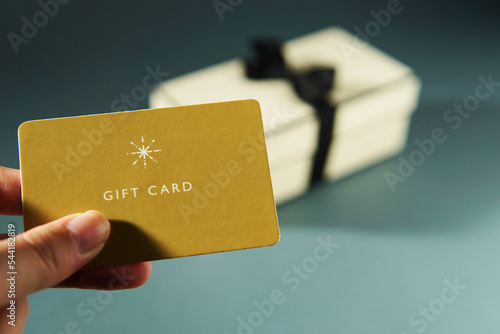 Hand holding a yellow gift card against a gift box background