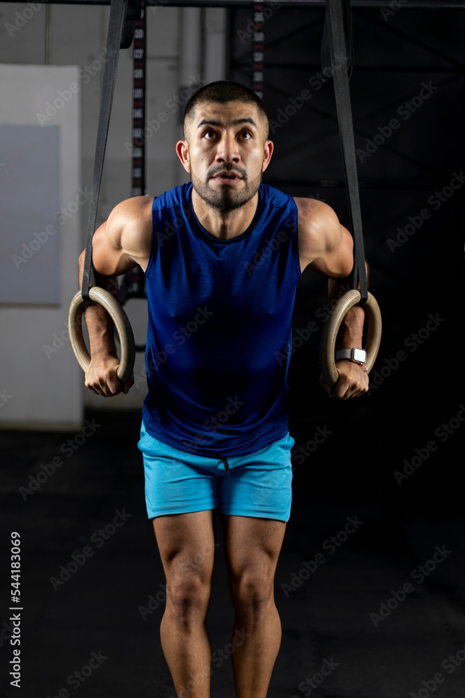 a Latino man in sportswear doing gymnastic exercises on some rings in a gym a Latino man in sportswear doing gymnastic exercises on some rings in a gym
