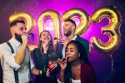 Multiracial people blowing party trumpets while celebrating new years eve in the club