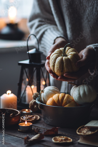 Autumn home composition with aromatic candles. Woman in wool sweater holding a pumpkin. Aromatherapy on a grey fall morning, atmosphere of cosiness and relax. Wooden dark background