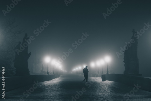 Photography Charles or Karlov bridge in Prague in early morning hours with a lot of fog and haze, with visible lights and no people