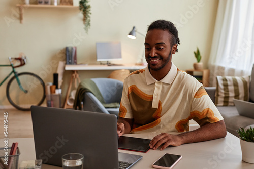 Portrait of smiling black man using pen tablet at home office workplace for digital design or photo editing