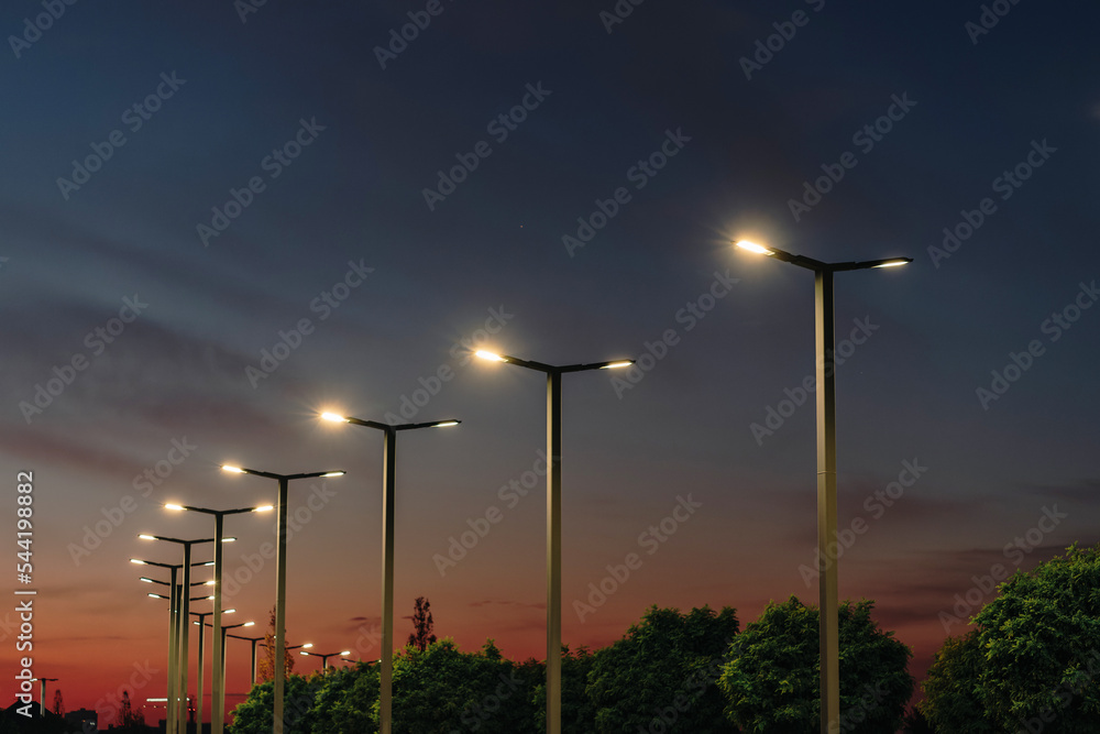 A modern street LED lighting pole. Urban electro-energy technologies. A row of street lights against the night sky - obrazy, fototapety, plakaty 