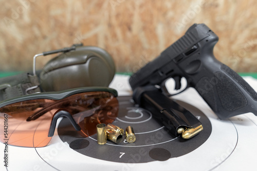 A pistol with cartridges, a target, goggles and headphones in a shooting range.