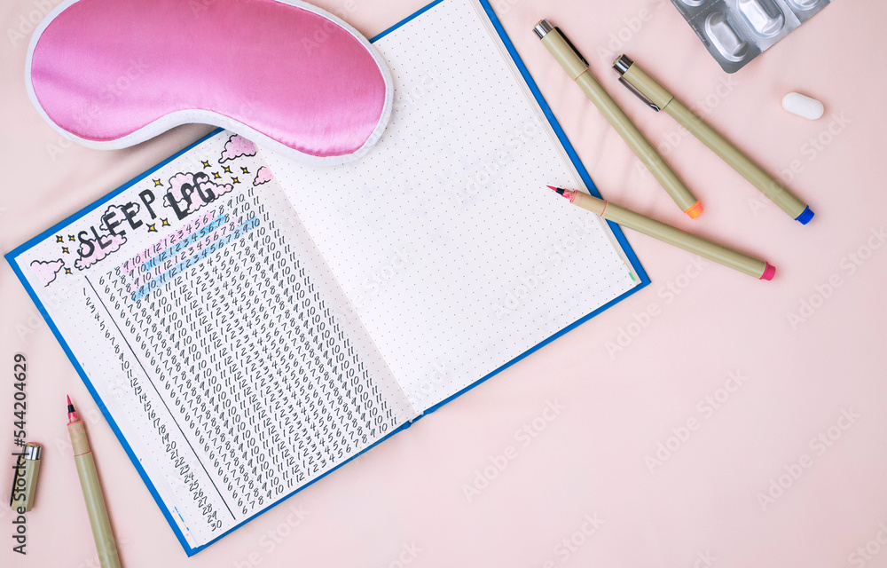 Sleeping mask, alarm clock and sleep tracker journal on pink pastel background. How to Use a Sleeping Log to Diagnose Insomnia Sleeping mask, alarm clock and sleep tracker journal on pink pastel background. How to Use a Sleeping Log to Diagnose Insomnia