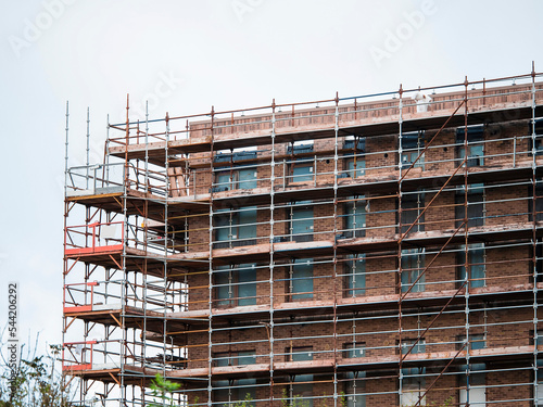 Construction site with modern building in scaffolding. Brick house, residential or commercial property development.