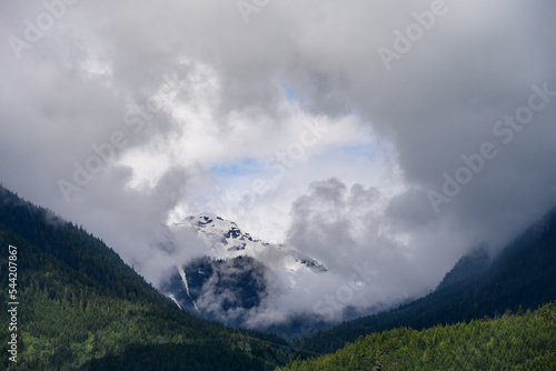 Distant mountain peak peaking out through clouds, forested hills in the foreground 