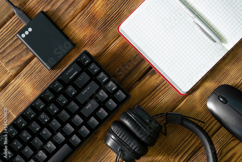 Photography Black computer keyboard, external ssd, headphones, notepad with pen and computer mouse on a table made of wooden pine boards