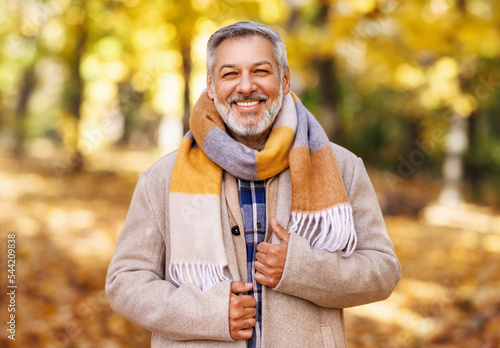 Happy positive mature man with broad smile in elegant clothes on an autumn walk in city park