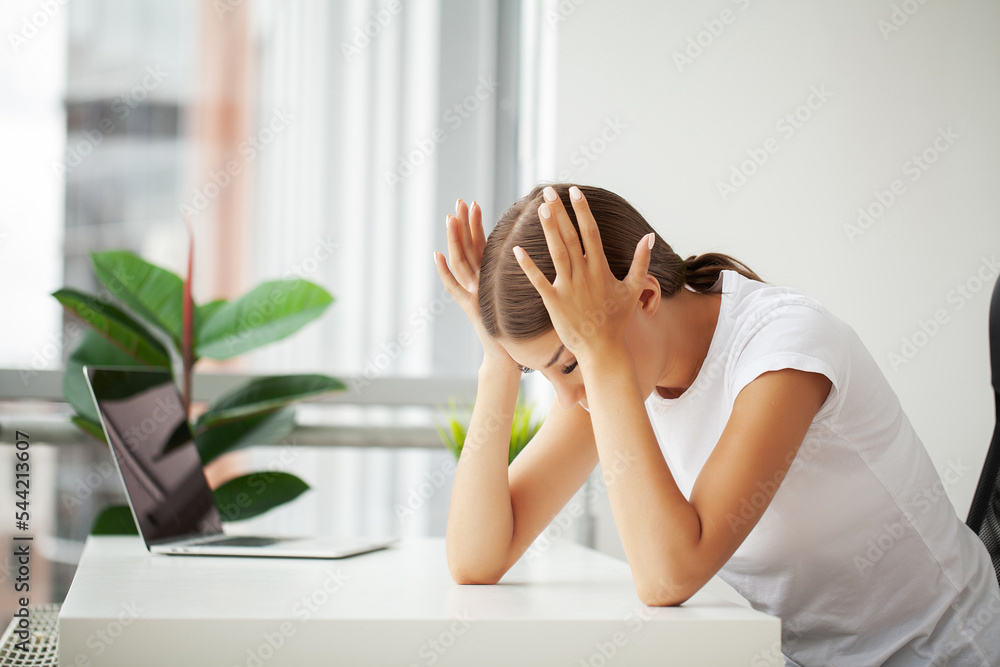 Beautiful stressed young office worker sitting at desk holding head because of pain in office Beautiful stressed young office worker sitting at desk holding head because of pain in office