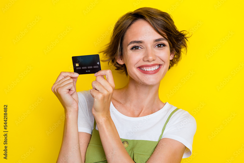 Closeup photo of young toothy beaming smile girl bob brown hair hold new debit card wireless payment technology isolated on yellow color background Closeup photo of young toothy beaming smile girl bob brown hair hold new debit card wireless payment technology isolated on yellow color background