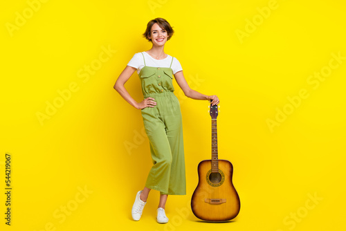 Full size photo of adorable young woman showing new guitar musical shop promo wear trendy khaki look isolated on yellow color background